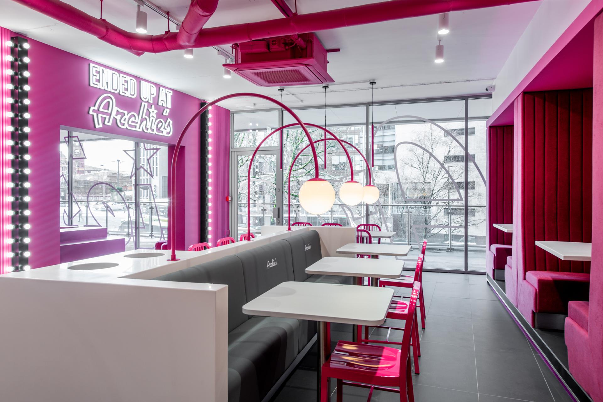 Vibrant cafe interior featuring pink decor, modern furnishings, and large windows for natural light.