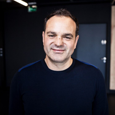 Lee Penson, CEO of PENSON, smiles confidently against a modern studio backdrop, reflecting his expertise in design and architecture.