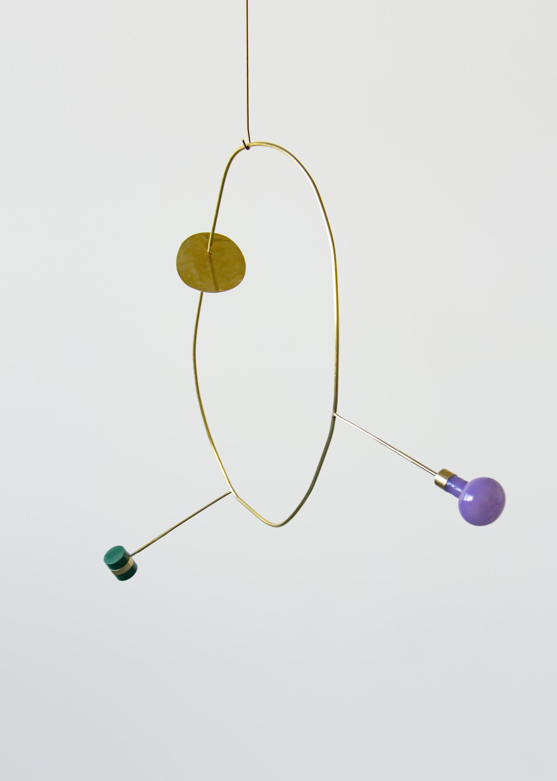 Modern mobile sculpture featuring brass and colorful bulbs, showcasing innovative design at the Crossovers by Adorno exhibition.