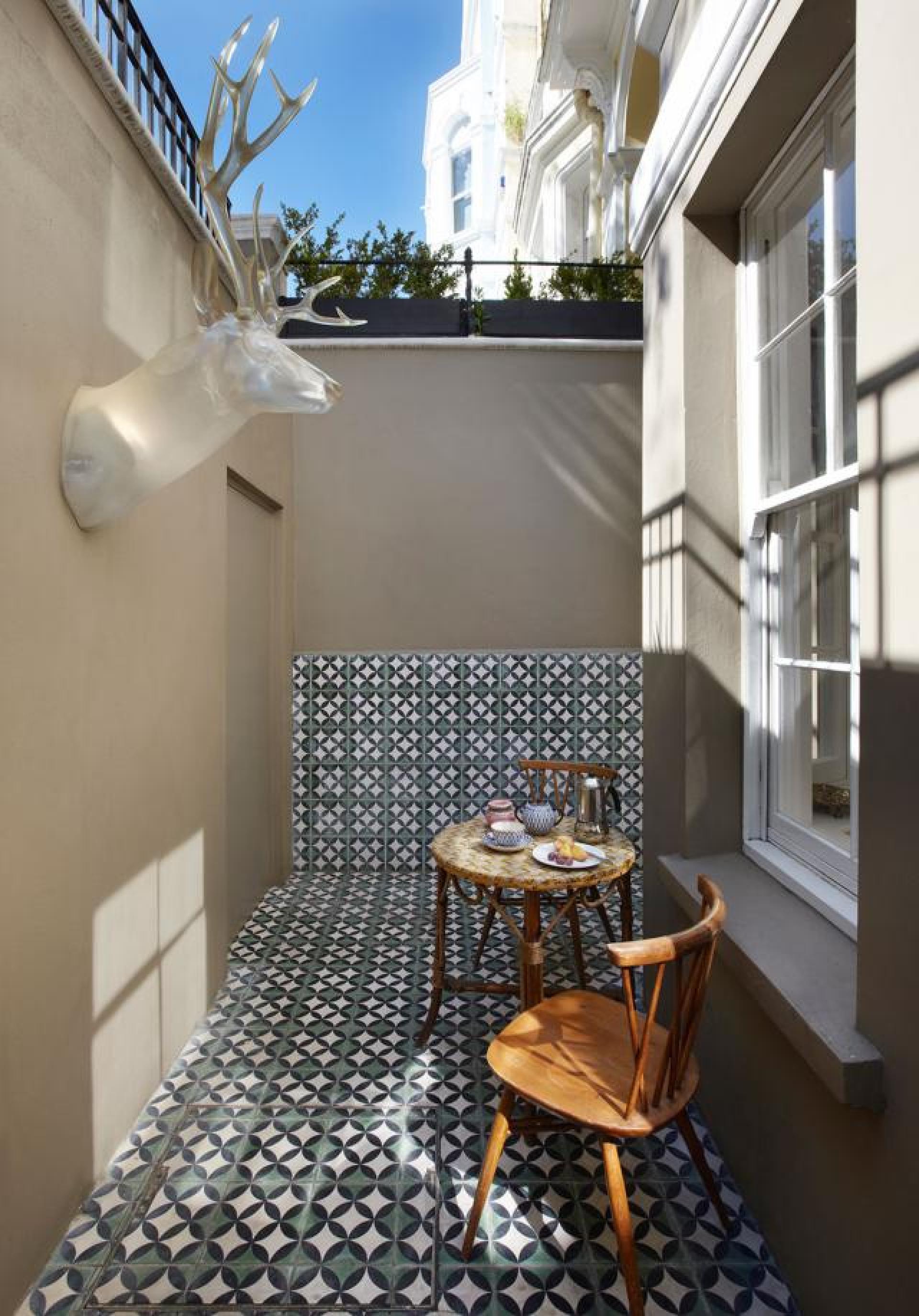 Elegant outdoor terrace featuring bold geometric tiles, a stylish table, and a deer head sculpture.