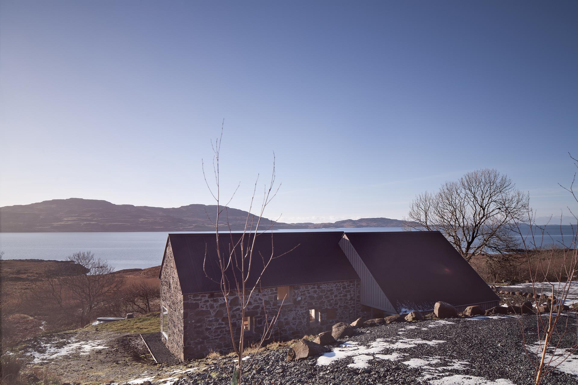 Restored croft on the Isle of Mull showcasing modern architecture with a scenic coastal backdrop and snow-capped landscapes.