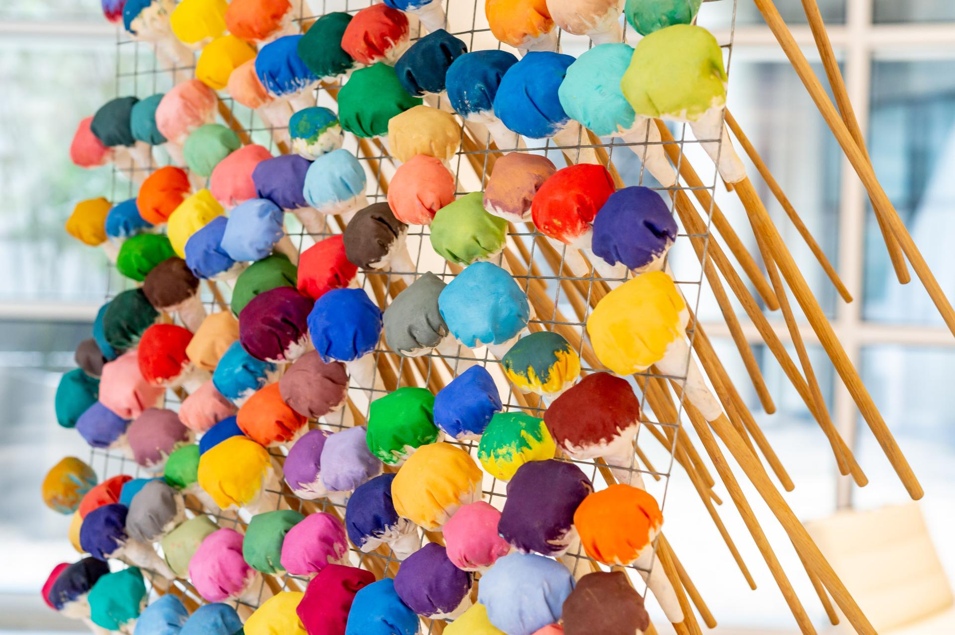 Colorful fabric pom-poms arranged on a grid frame, showcasing British textile artist Anna Ray's innovative weaving tribute.