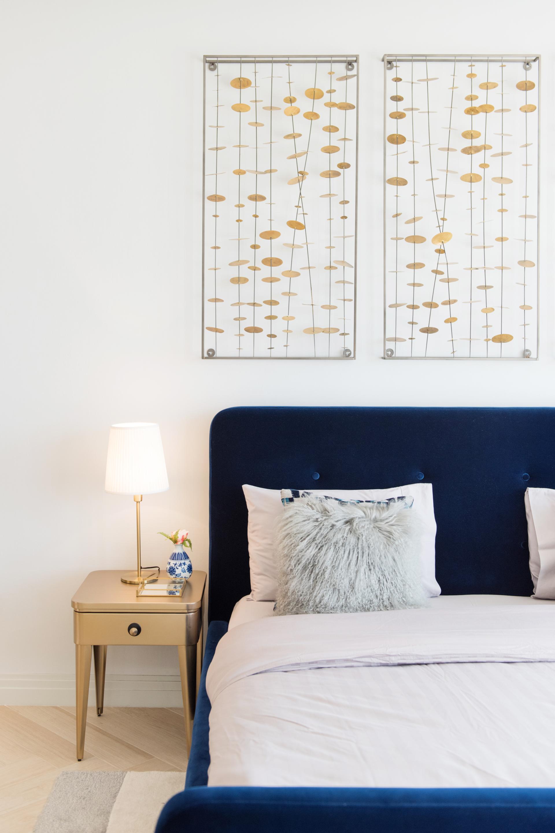 Minimalist bedroom design featuring a navy blue upholstered headboard, gold accents, and artistic wall decor in Palm Jumeirah, Dubai.