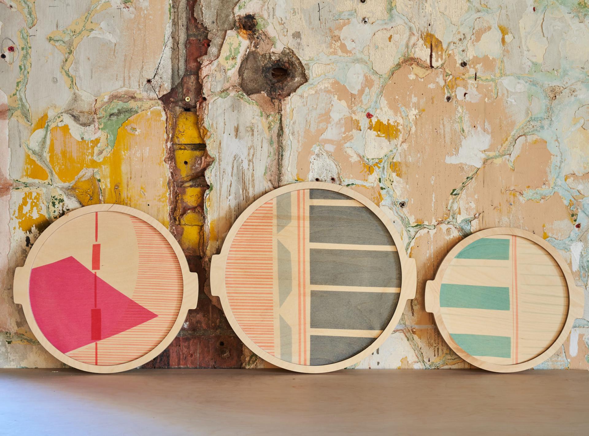 Colorful wooden trays with geometric designs displayed against a rustic wall, highlighting innovative craft design.