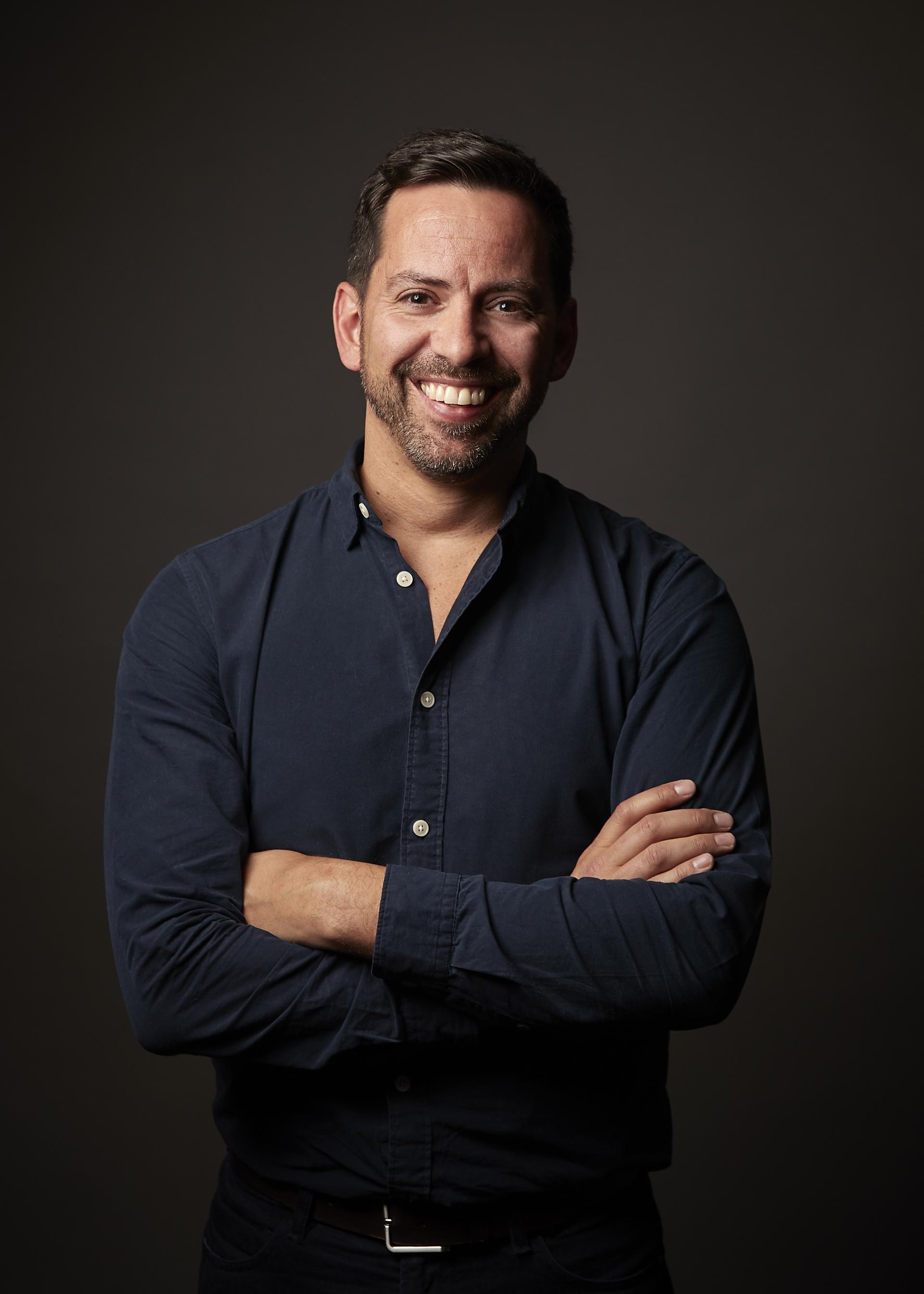 Smiling man in a dark shirt posing confidently, promoting Nulty's online masterclass series for interior designers.