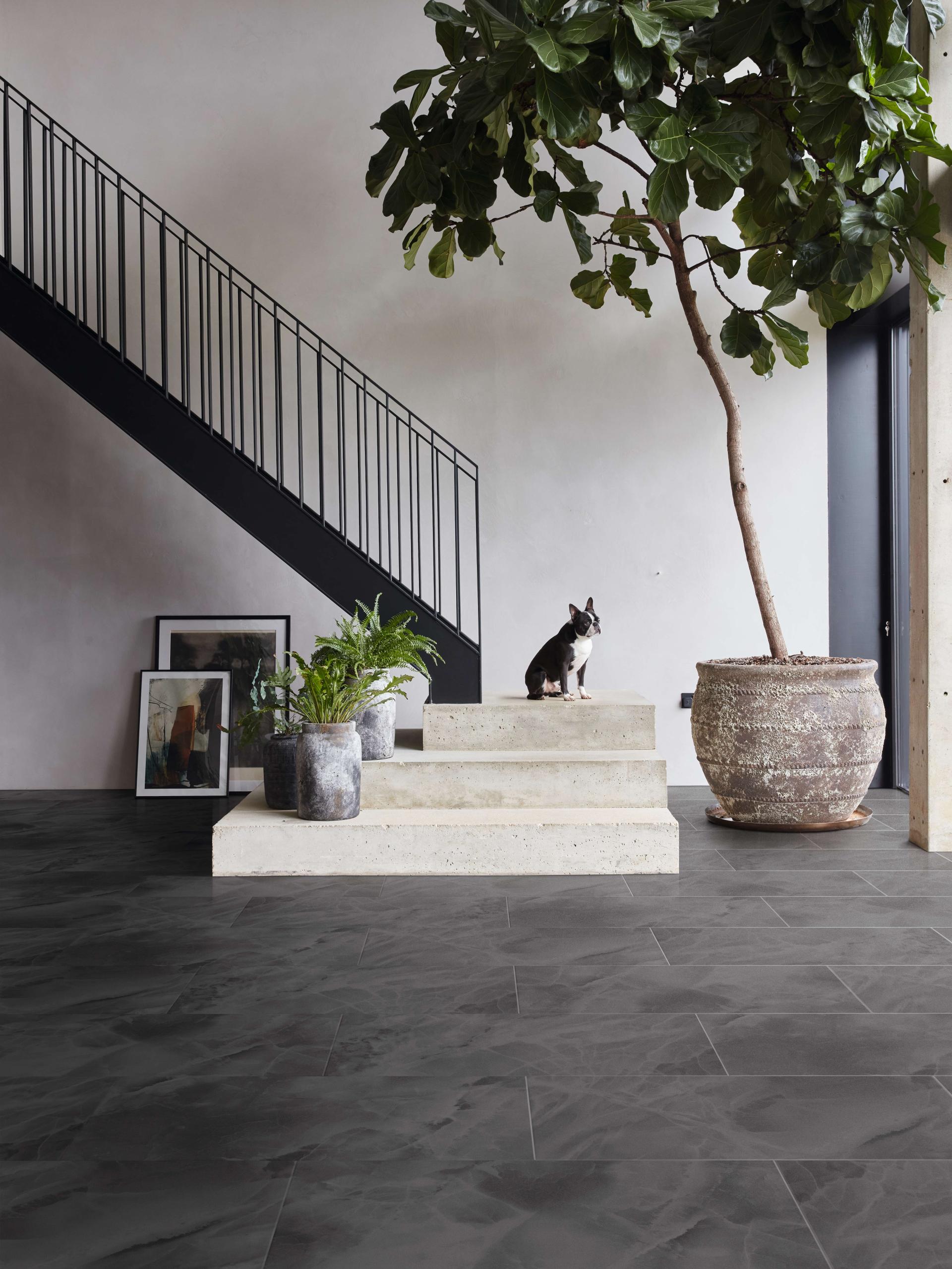 Stylish interior featuring Karndean Designflooring's luxurious stone tiles, a staircase, greenery, and a dog.
