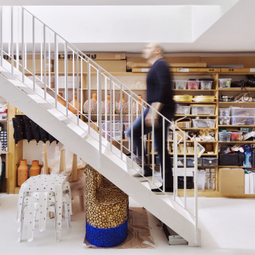A person walks up a modern staircase in a creative studio filled with art supplies and unique furnishings.