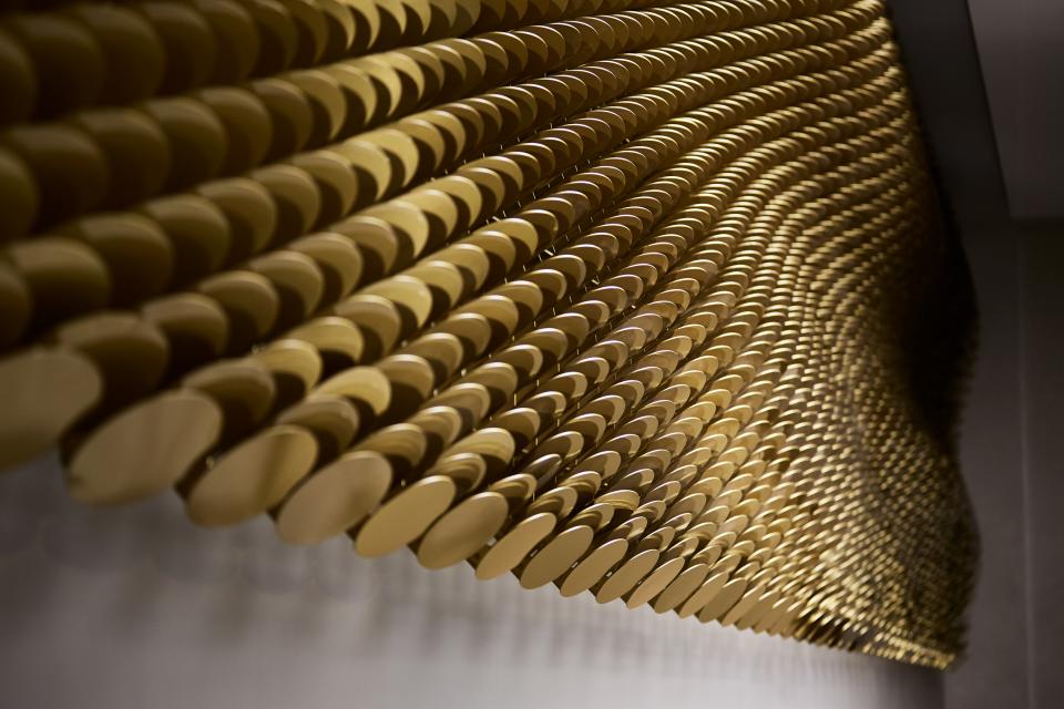 Brass louvres create a wave-like architectural artwork, highlighting light play and texture in Giles Miller's The Veil.