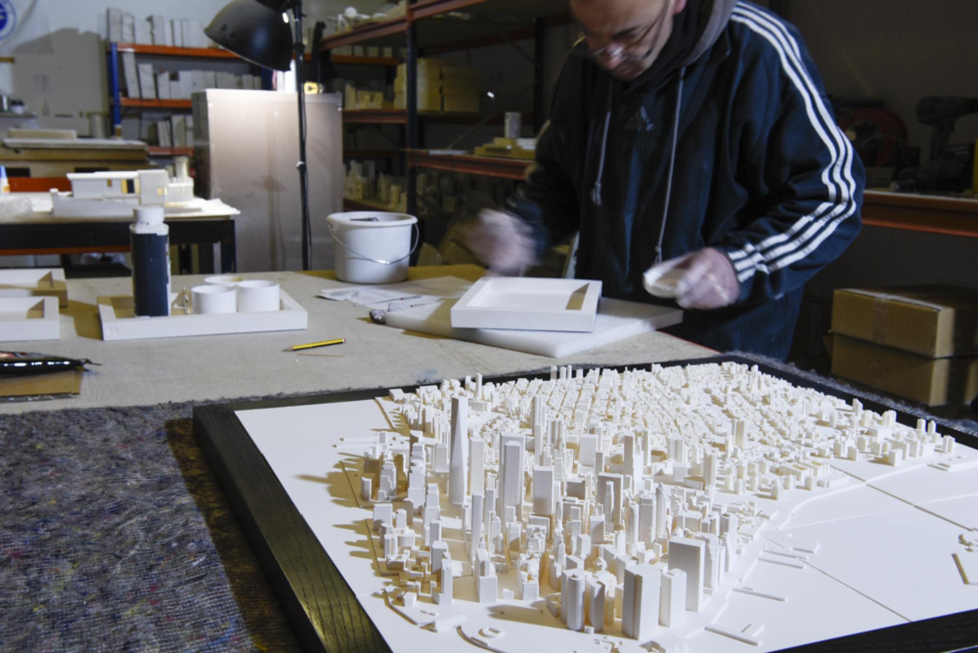 Artist working on a detailed three-dimensional model of a cityscape, showcasing intricate urban features and architecture.