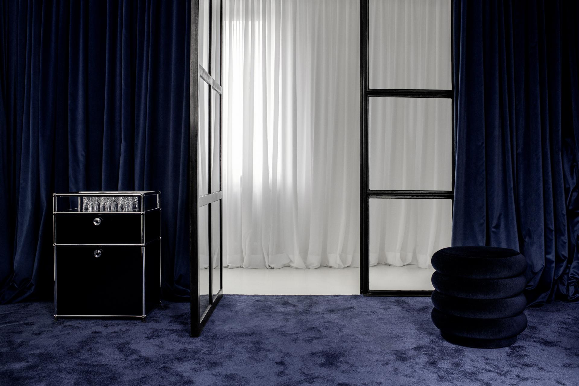 Elegant interior design featuring a sleek black drawer unit, velvet curtains, and a modern stool in a stylish atelier.