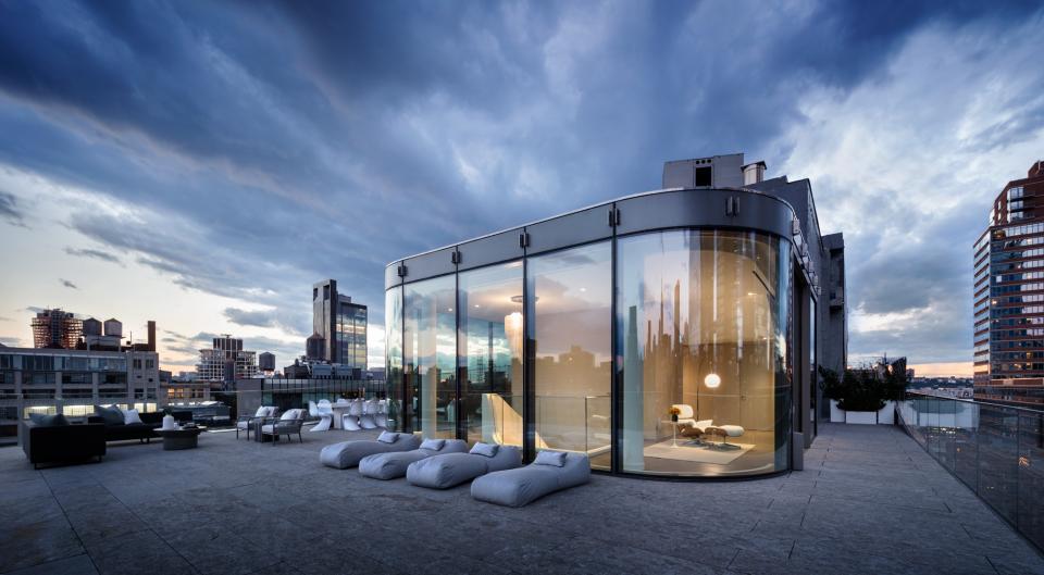 Stylish luxury penthouse terrace designed by Zaha Hadid, featuring sleek glass walls and stunning city skyline views.