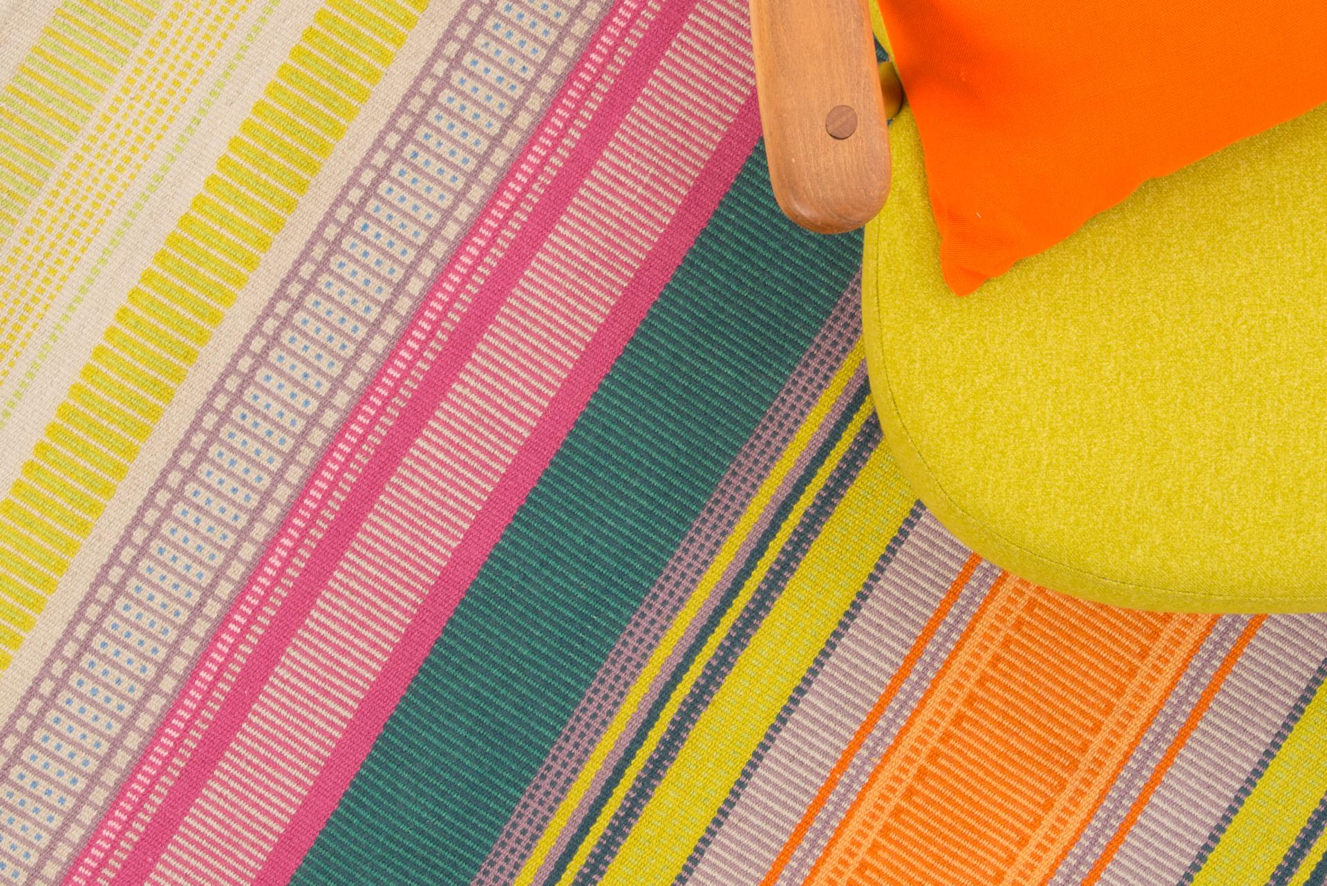 Vibrant patterned rug with bold stripes and a yellow chair featuring an orange cushion, showcasing modern British design.