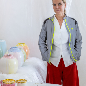 Coralla Maiuri stands in her studio surrounded by colorful ceramic vases and artistic tableware, showcasing her experimental design style.