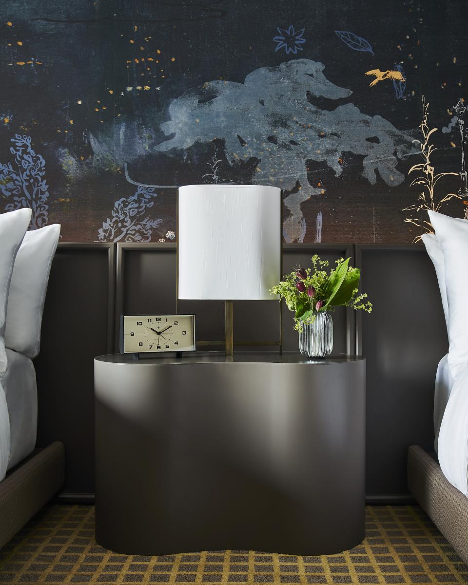 Stylish bedside table with a lamp, clock, and fresh flowers against an artistic dark wall in Park Lane New York.