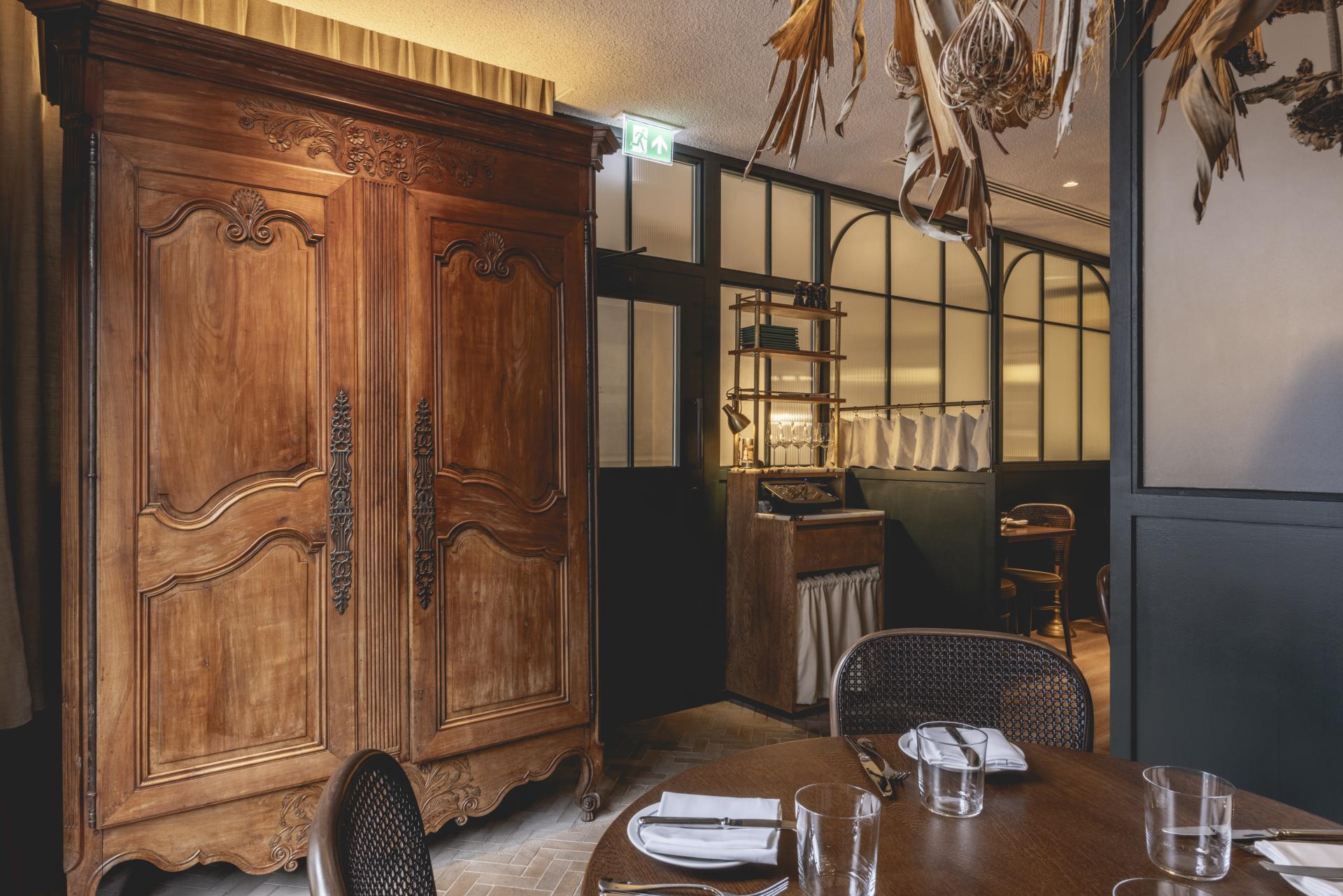 Rustic wooden armoire and elegant dining table set in Studio Found's Fitzrovia restaurant with Parisian decor elements.
