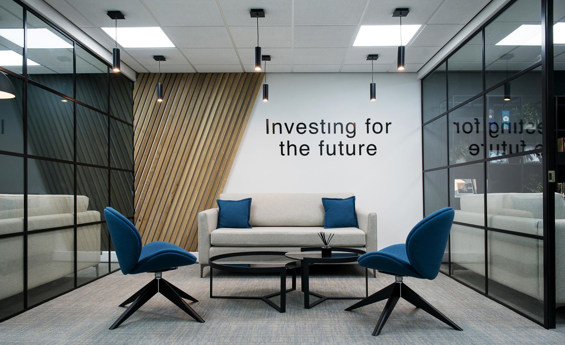Modern workspace featuring a stylish sofa and blue accent chairs with a wall inscription promoting future investment.