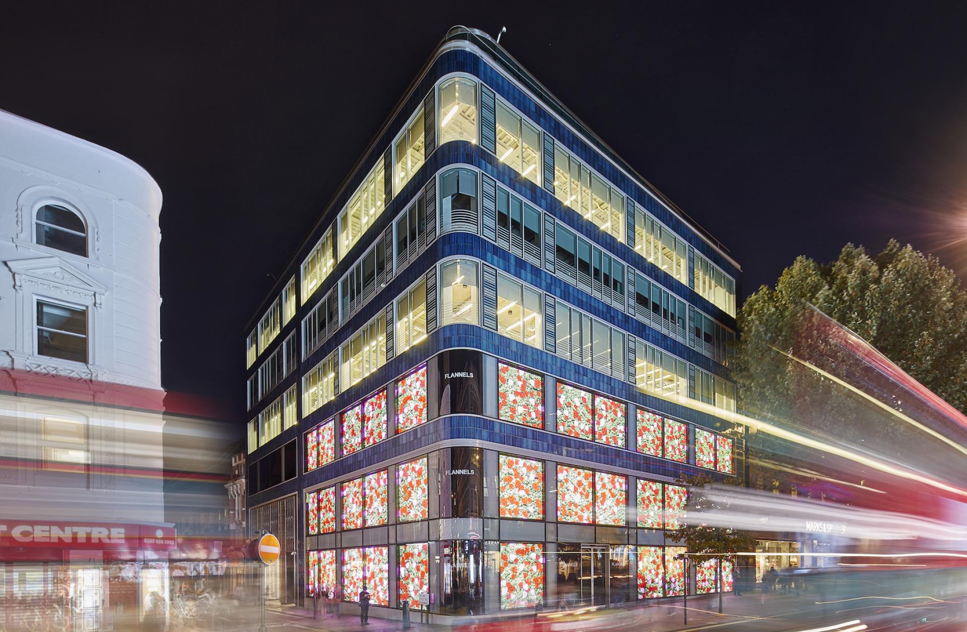 New London offices of Sports Direct International, showcasing modern architecture by PENSON with vibrant illuminated windows at night.