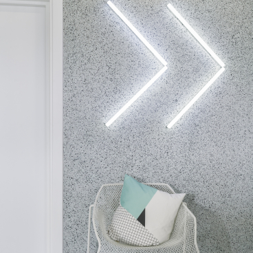 Modern workspace design featuring a white chair with geometric pillows and creative wall lighting in a textured gray setting.