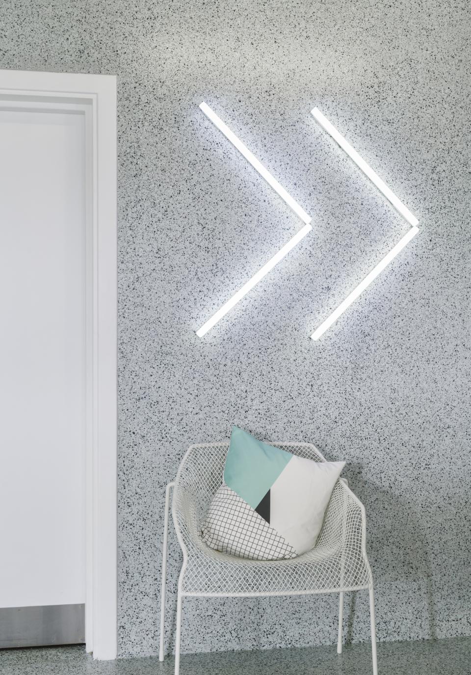 Modern workspace design featuring a white chair with geometric pillows and creative wall lighting in a textured gray setting.