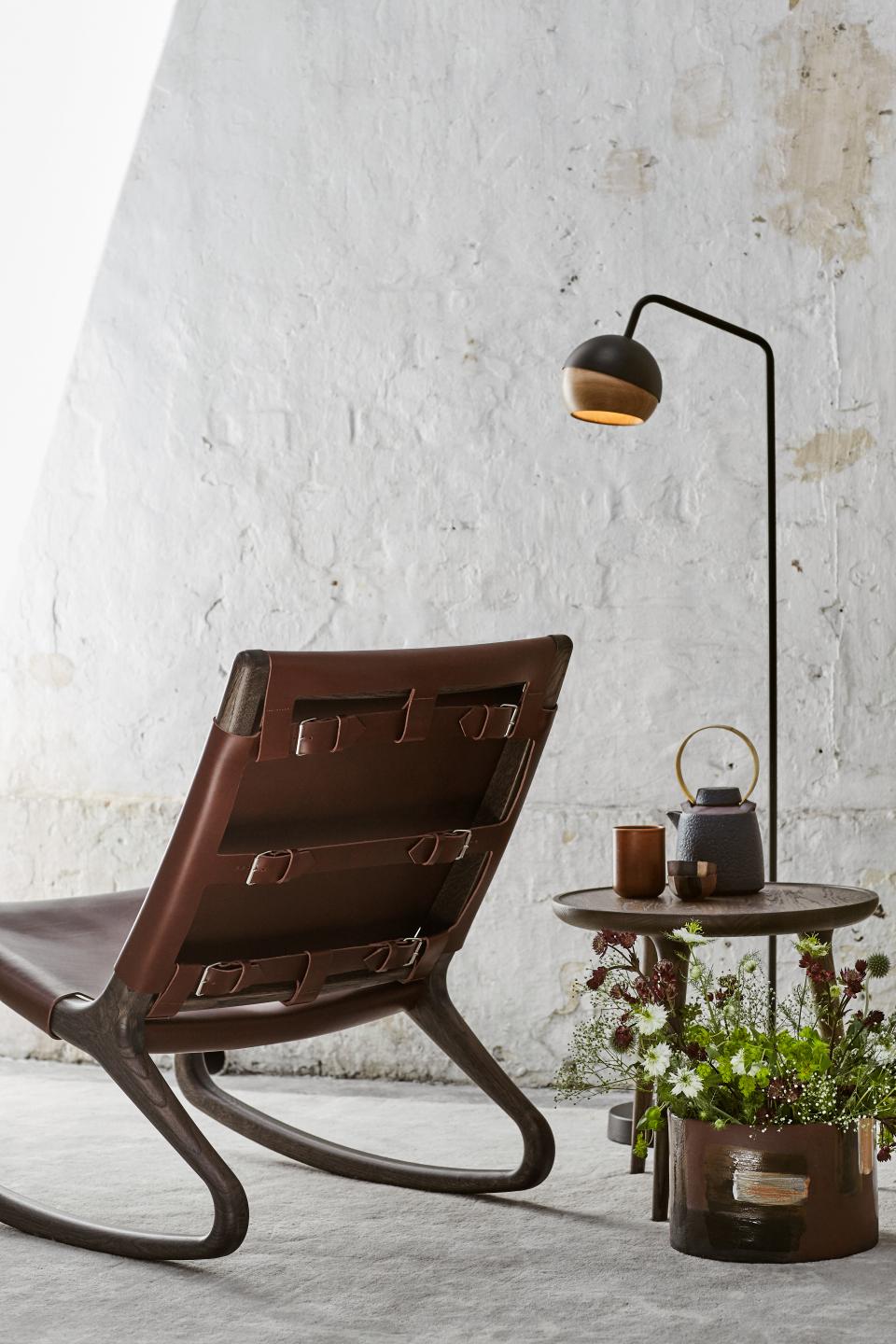 Elegant rocking chair by Mater, designed by Shawn Place, surrounded by decorative items and flowers in a modern interior setting.