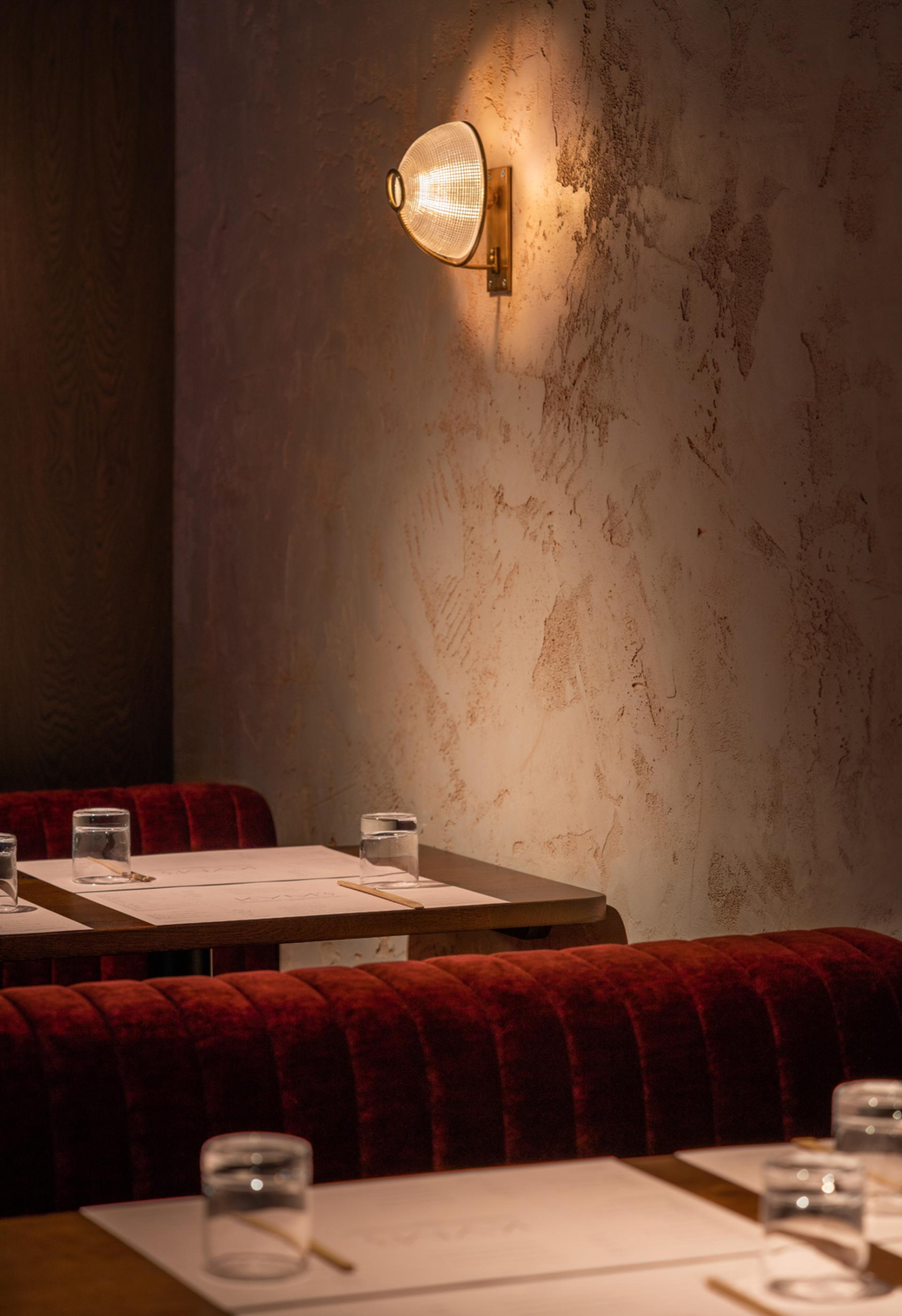 Interior view of Chef Andrew Wong's restaurant, featuring wooden tables, red velvet seating, and stylish wall lighting.