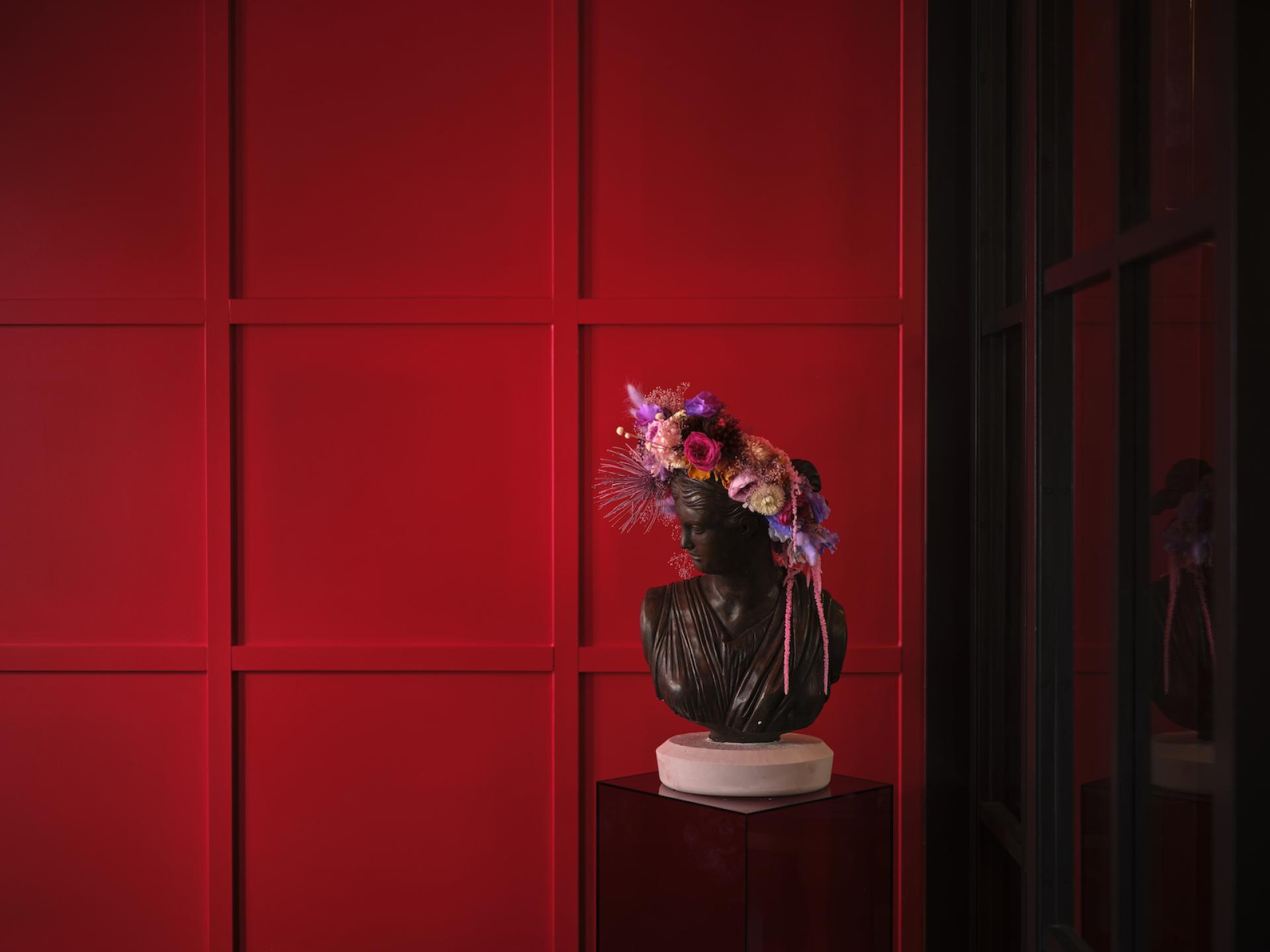 Bust sculpture adorned with vibrant floral crown, set against a bold red wall at Naumi Studio Hotel, Wellington.