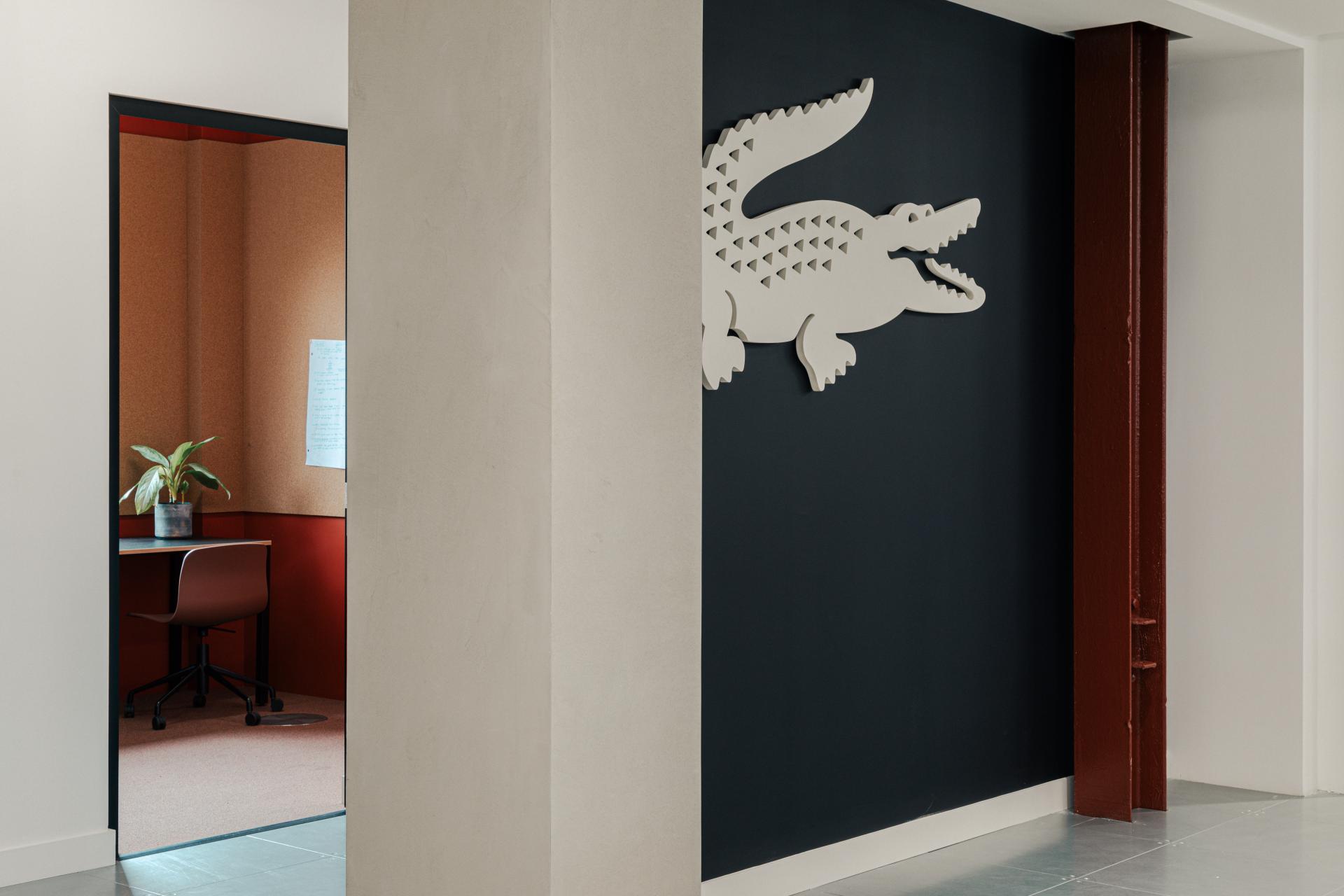 Lacoste-inspired workspace featuring stylish design elements, including a dark wall with a crocodile logo and modern office space.