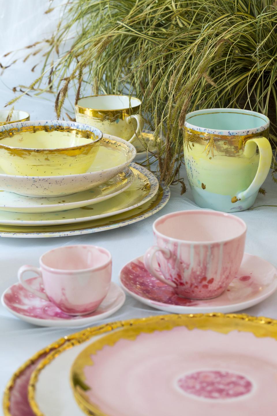 Hand-decorated ceramic and porcelain tableware by Coralla Maiuri, featuring vibrant colors and artistic patterns, displayed with greenery.
