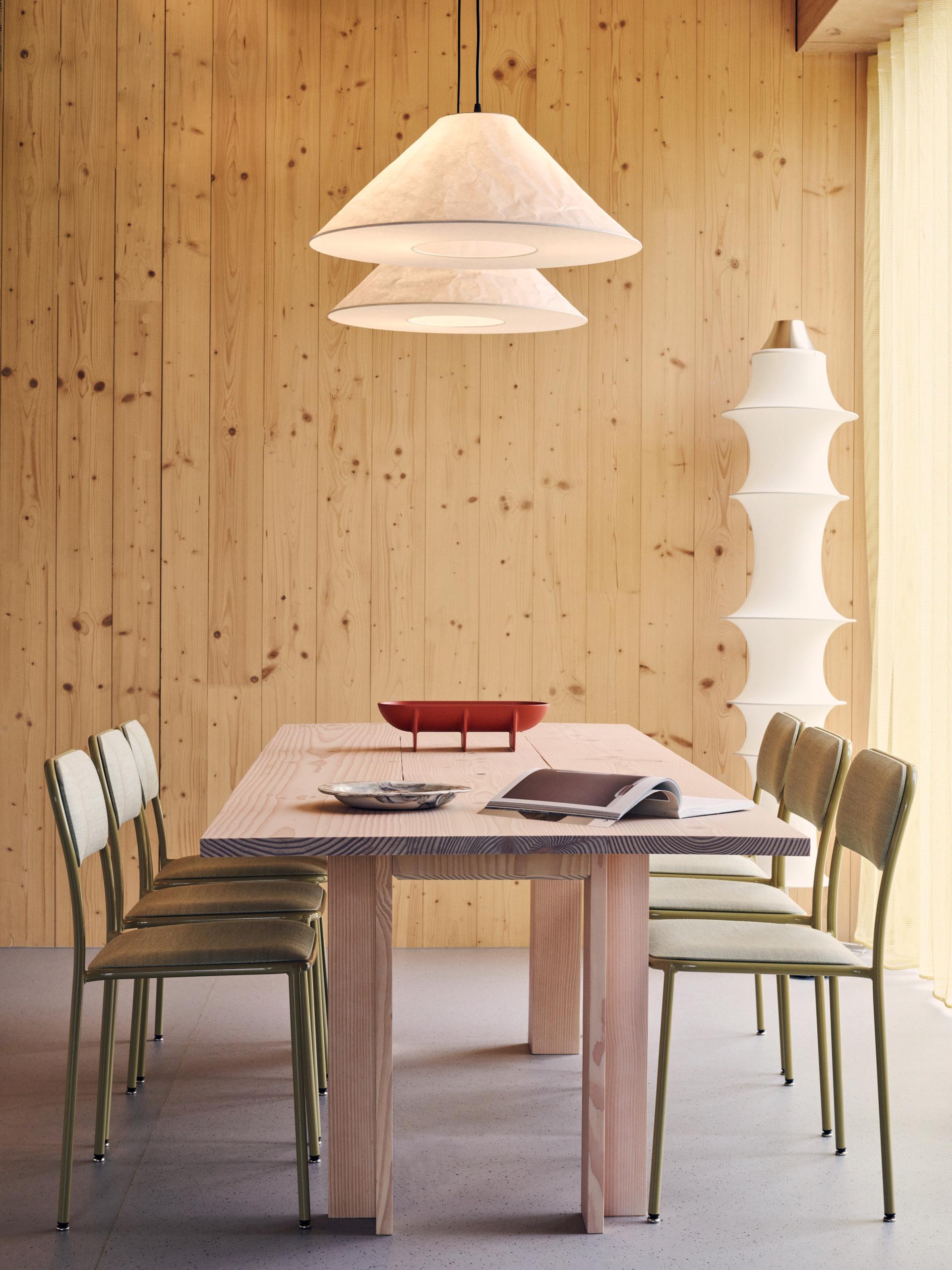 Stylish dining area featuring a wooden table, green chairs, and elegant lighting, highlighting sustainable design elements.
