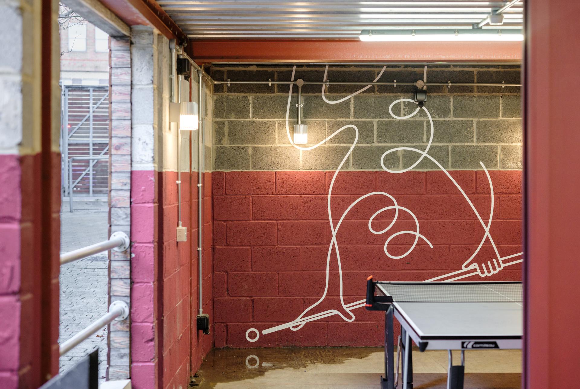 Colorful mural on a wall featuring abstract figures, with a table tennis setup in the iQ East Court amenities.