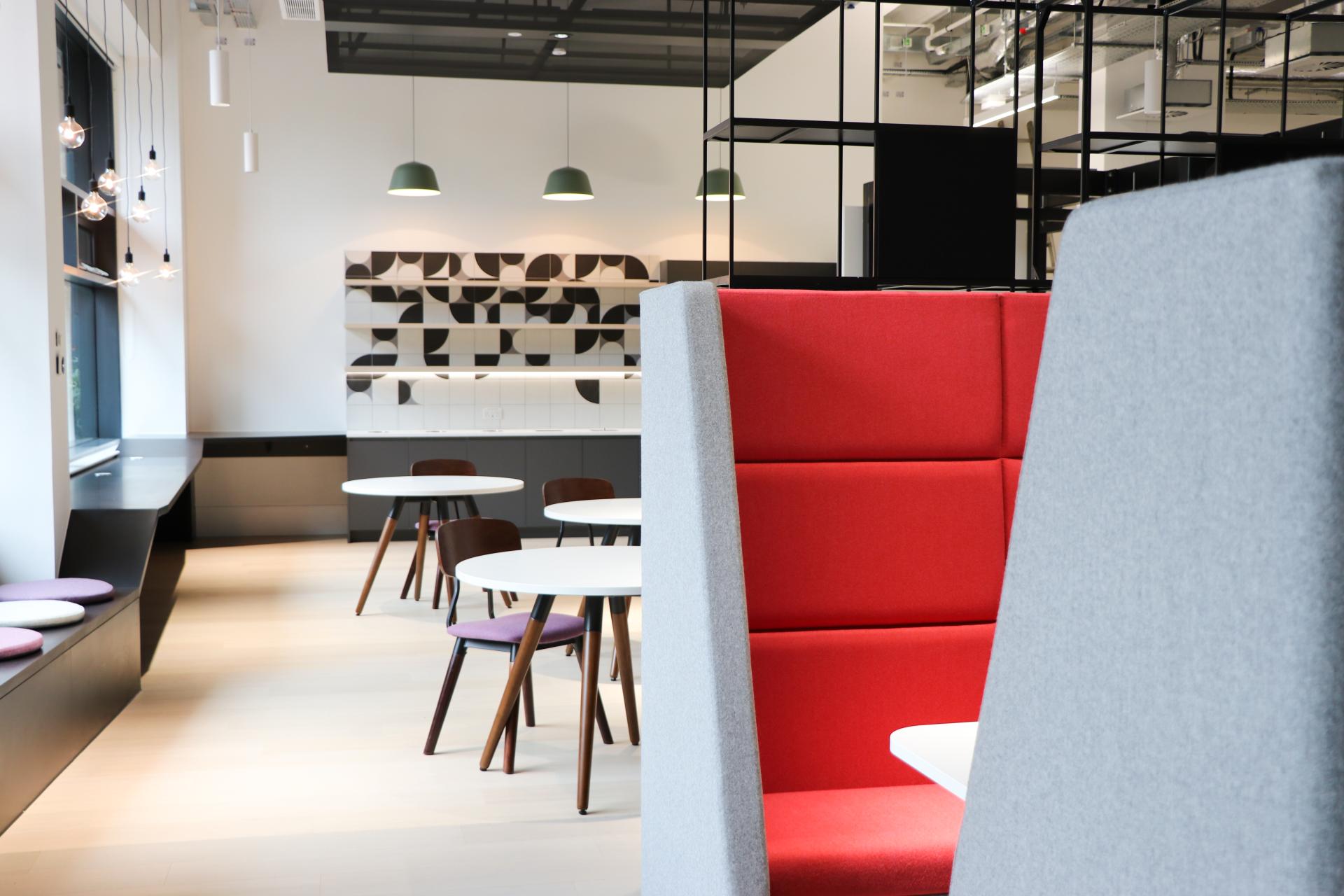 Modern workspace featuring minimalist design elements, including a red booth, white tables, and geometric wall tiles.