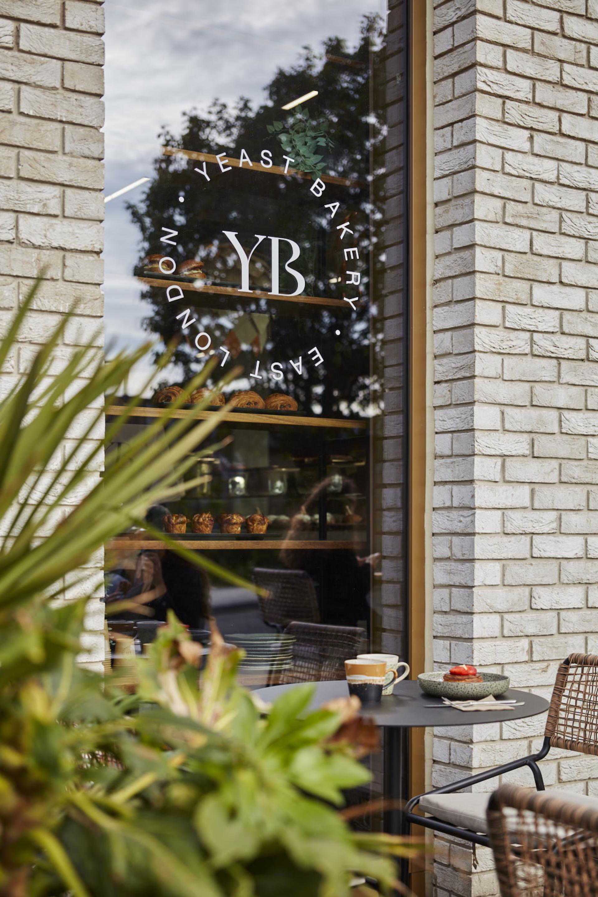 Modern cafe setting at Yeast Bakery, featuring a logo, pastries in view, and a table with coffee and dessert.