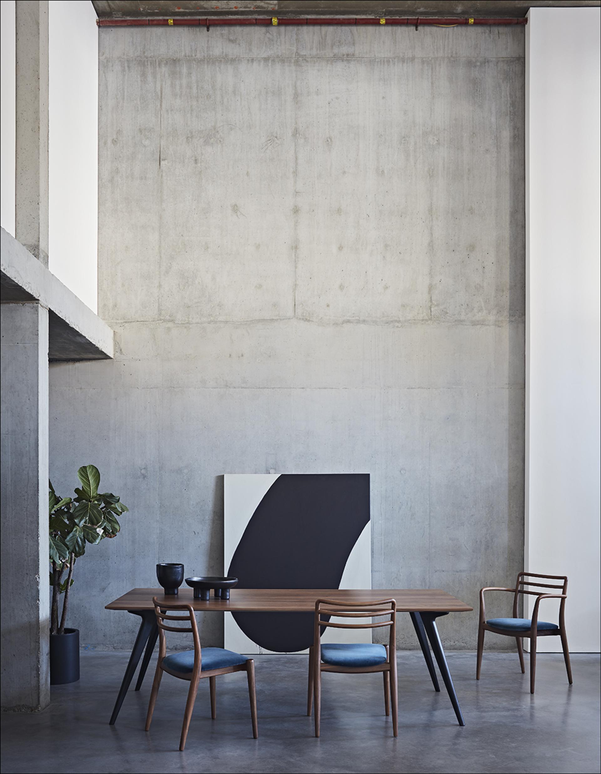 Modern dining space featuring a stylish wooden table, upholstered chairs, and contemporary art against a concrete wall.
