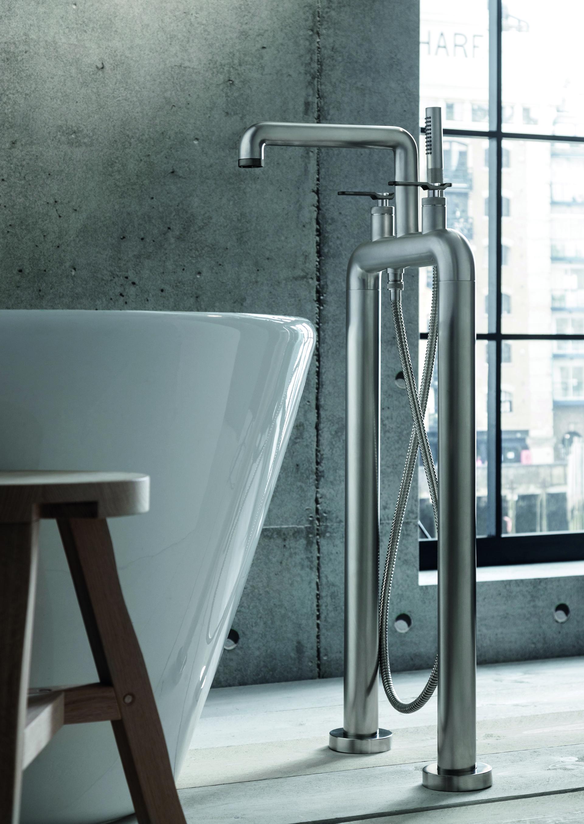 Sleek industrial-style brass freestanding faucet next to a modern freestanding bathtub, showcasing Crosswater's UNION Mixage collection.