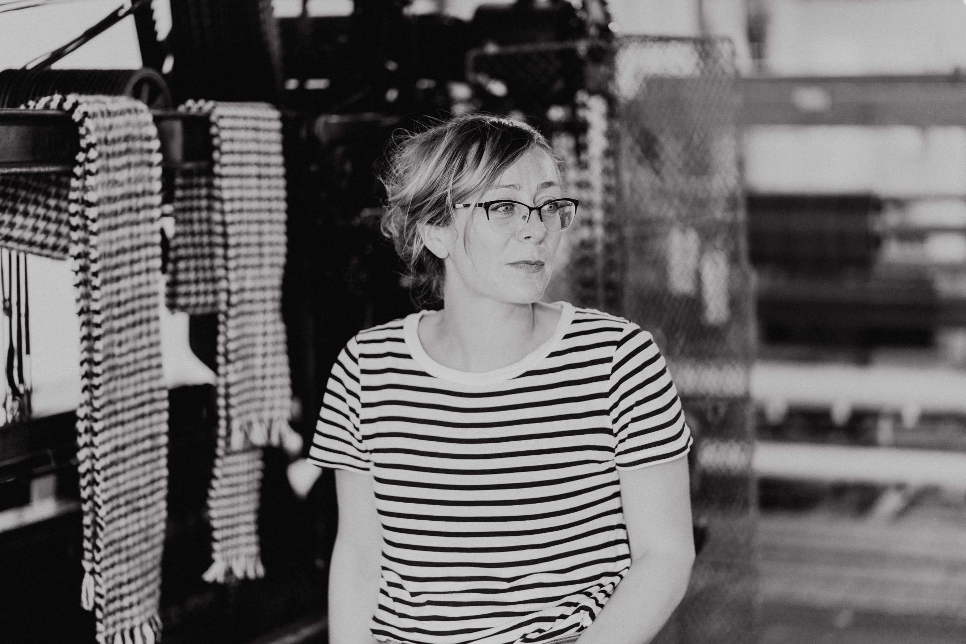 Craft artist in Glasgow wearing a striped shirt, seated with woven textiles in the background, embodying creative craftsmanship.