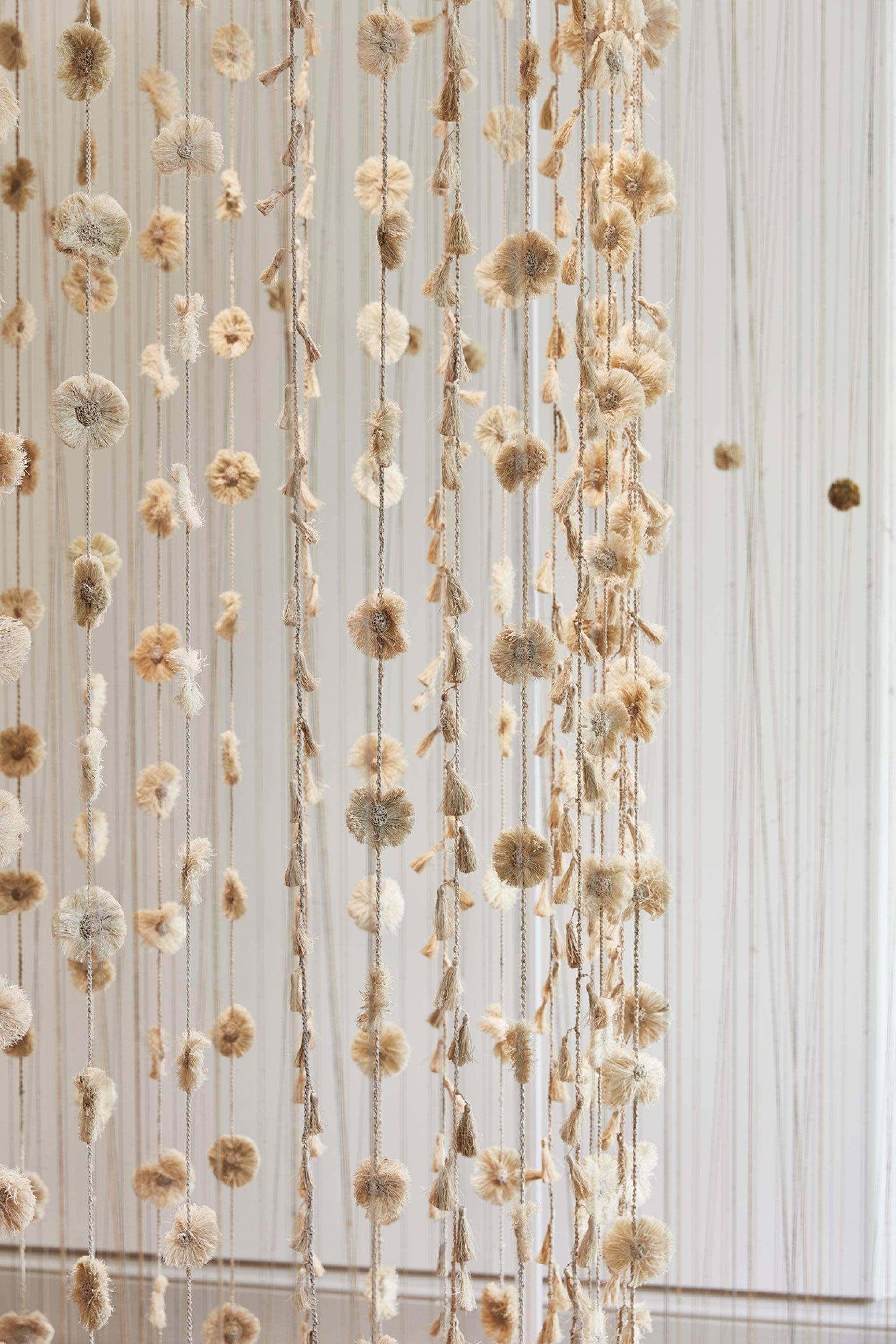 Delicate textile installation featuring hanging fabric flowers and tassels at the London Design Biennale 2023.