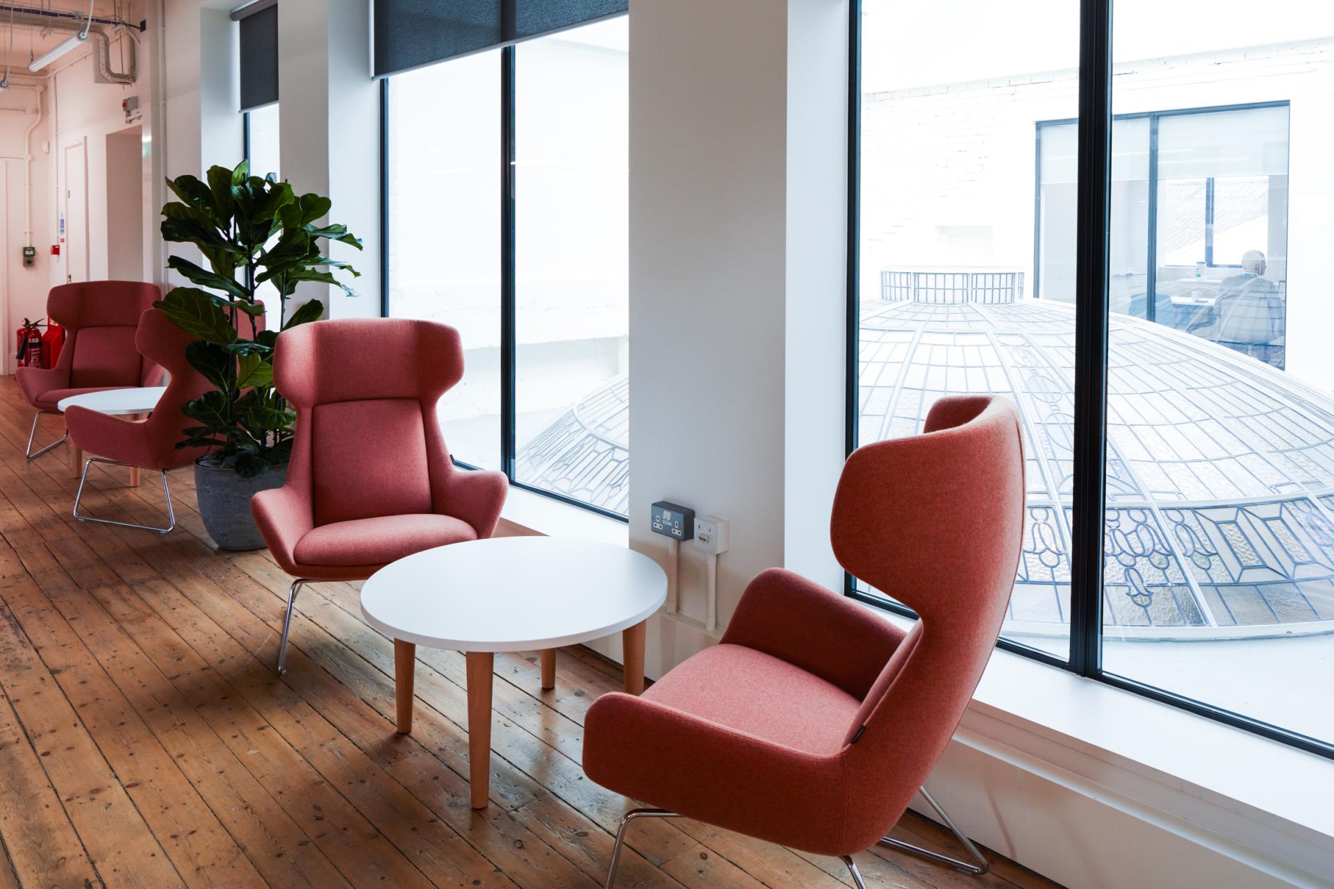 Modern workspace with pink chairs, a round table, and natural light from large windows at Queen Mary University.