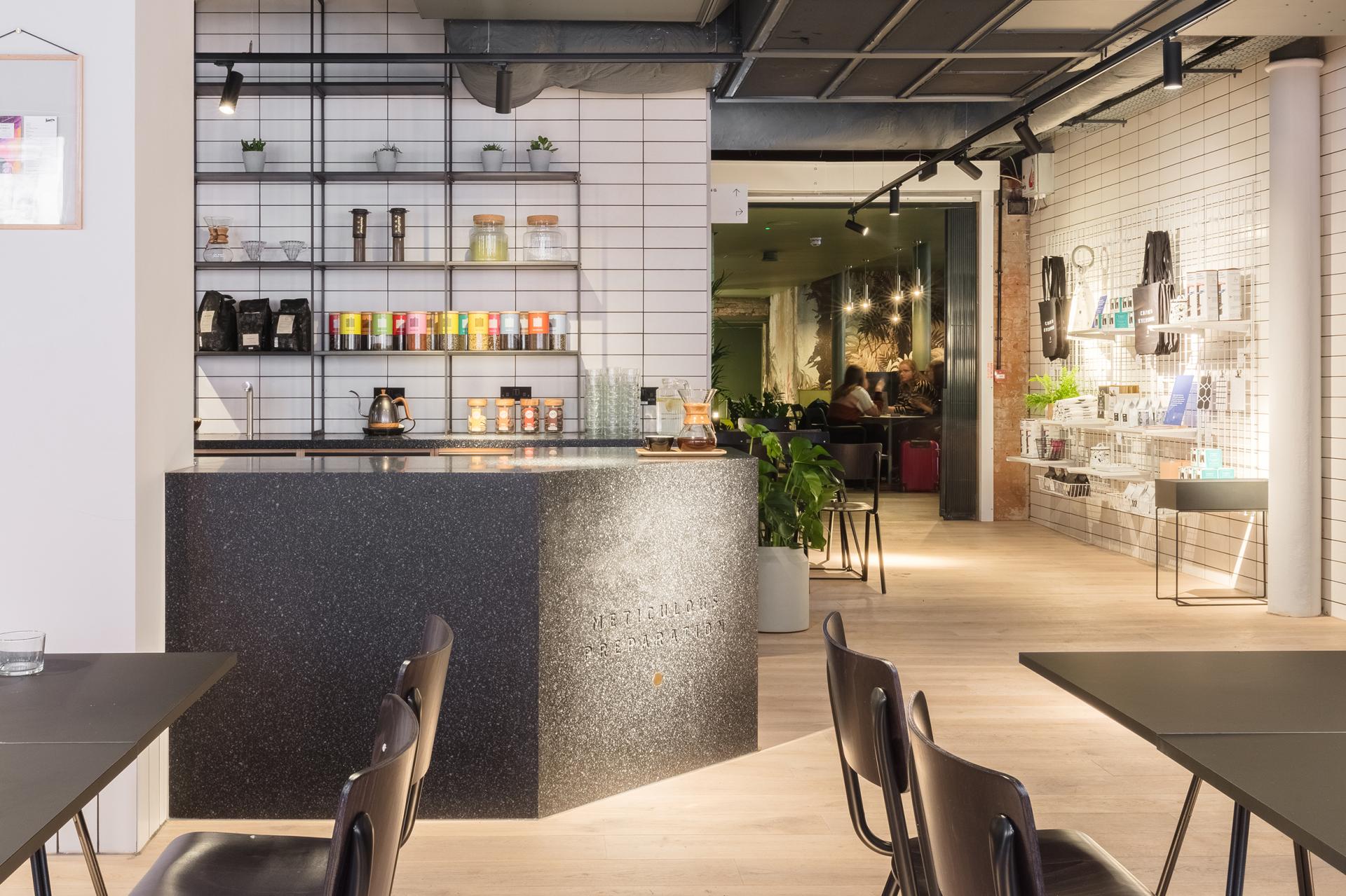 Modern cafe interior featuring a stylish black counter, shelves of colorful teas, and a welcoming atmosphere for design inspiration.