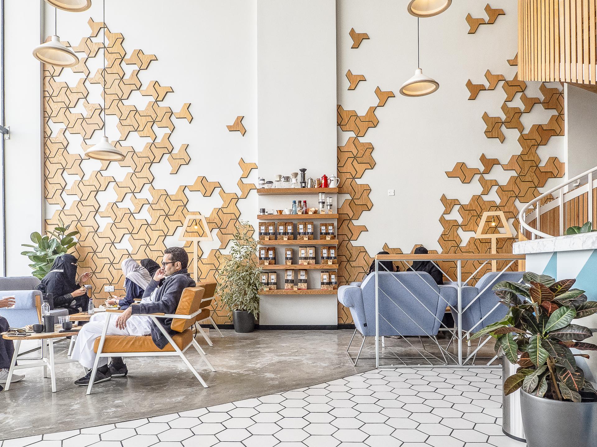 Stylish interior of Brew92 café featuring wood wall art, cozy seating, and patrons enjoying coffee in Saudi Arabia.