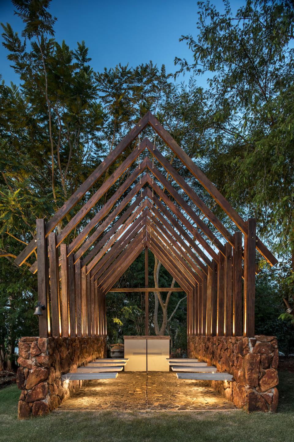 Stylish wooden structure with stone base and ambient lighting, surrounded by lush greenery at The Lake House in Brazil.