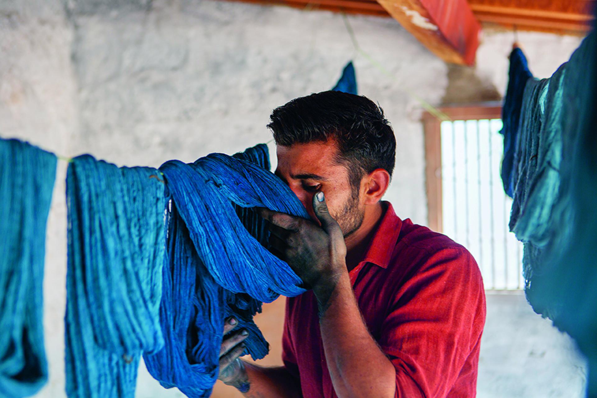 Textile artisan intensely examining vibrant blue dyed fabrics in a traditional workshop, showcasing the artistry of color and textiles.