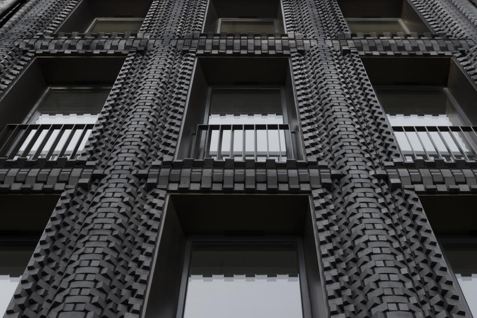 Innovative brick facade design of a modern building showcasing textured black bricks and large windows, reflecting contemporary architecture.