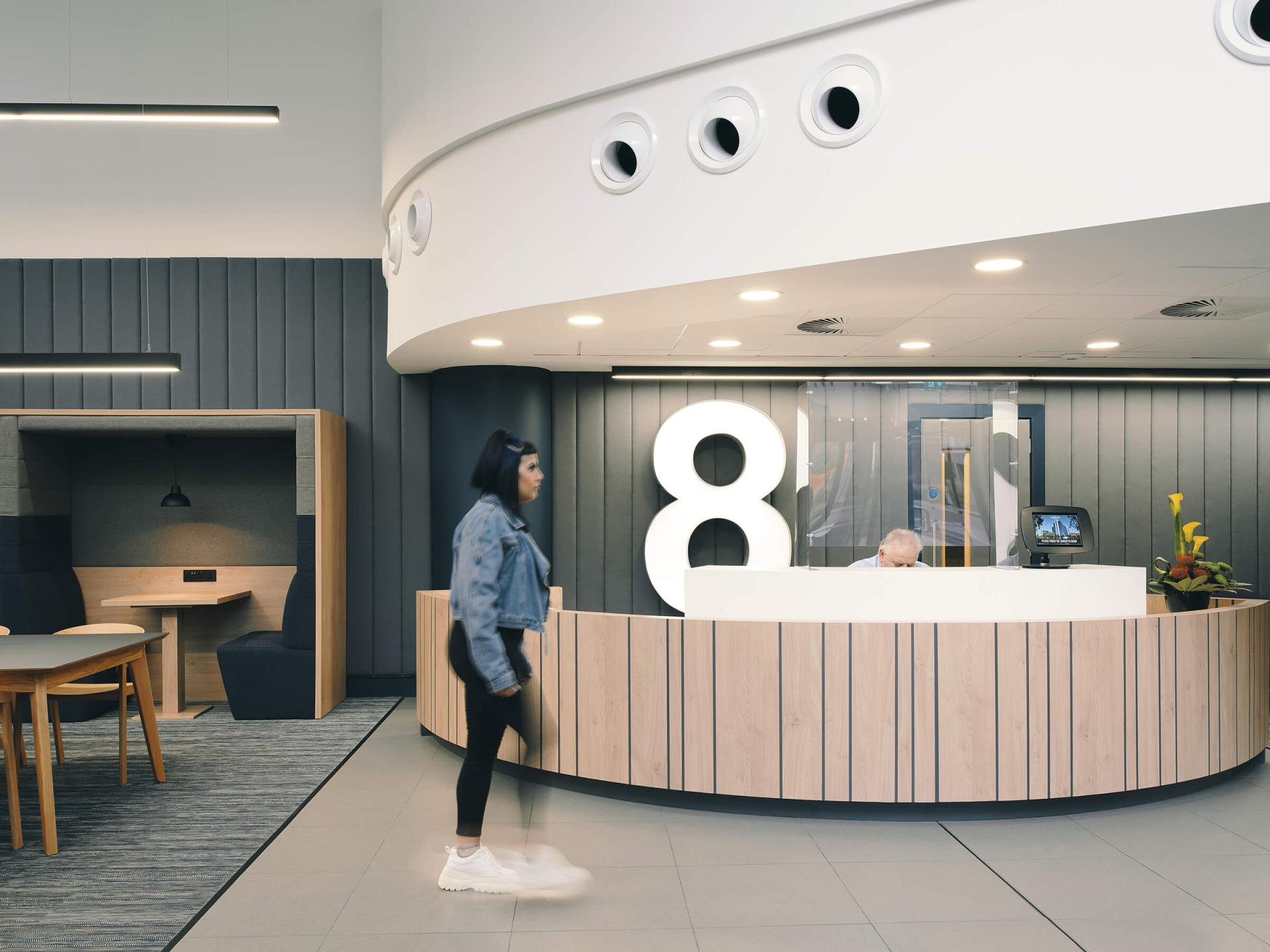 Modern reception area featuring sustainable design elements, a seated receptionist, and stylish wooden finishes.
