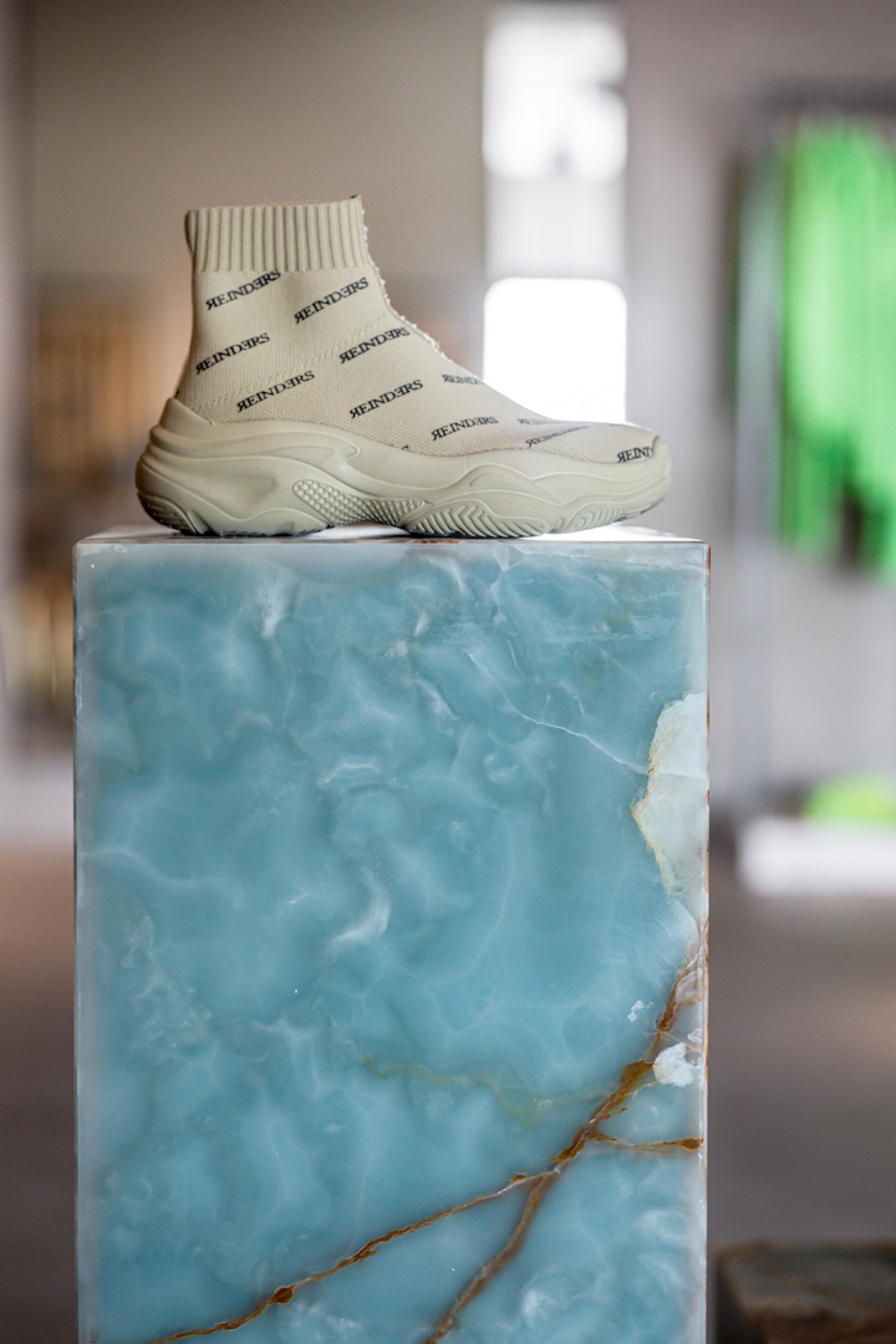 Stylish Reinders sneaker displayed on a striking blue marble pedestal in a modern showroom setting.