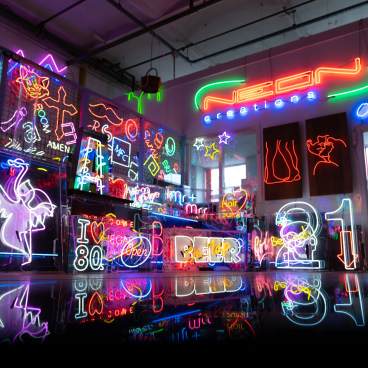 Colorful neon signs illuminate a creative workspace, showcasing various designs and messages related to neon art and decor.