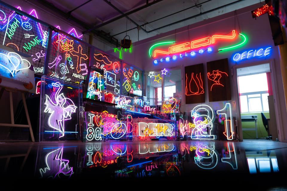 Colorful neon signs illuminate a creative workspace, showcasing various designs and messages related to neon art and decor.