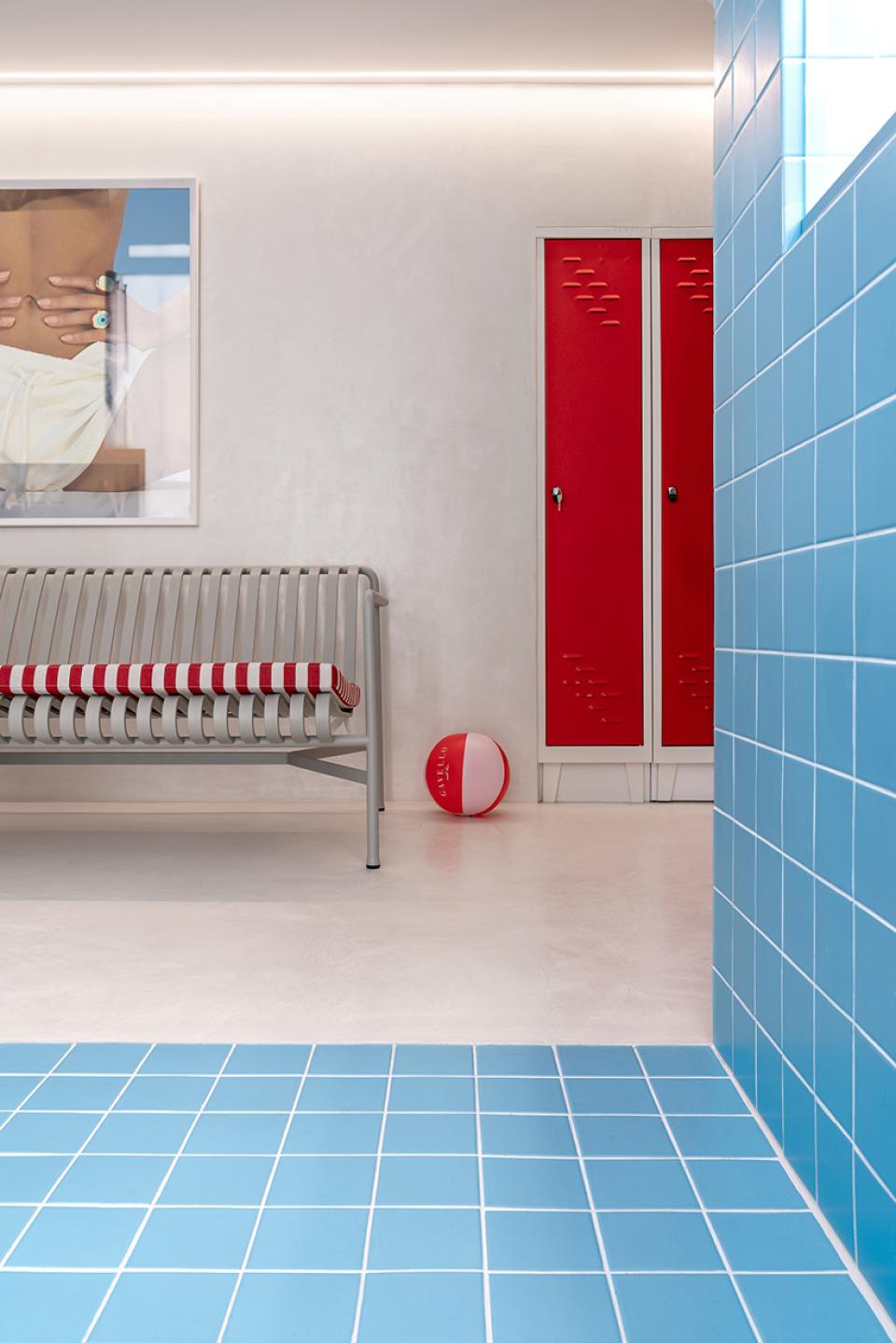 Bright blue tiled floor and a red-striped bench create a playful, pool-like atmosphere in a Mykonos jewellery shop.