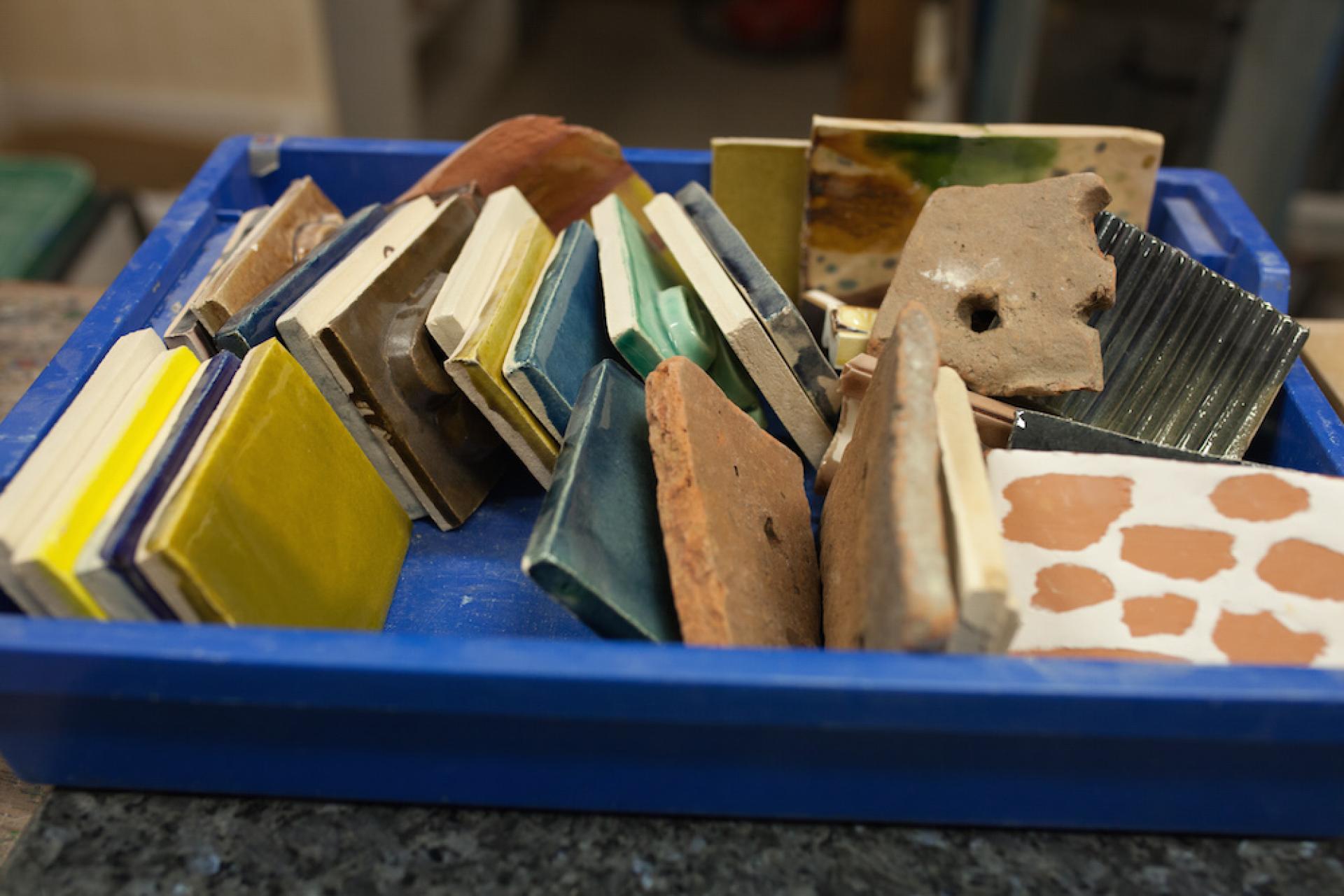 Colorful ceramic samples and tiles arranged in a blue tray, reflecting Matthew Raw's artistic exploration of clay.