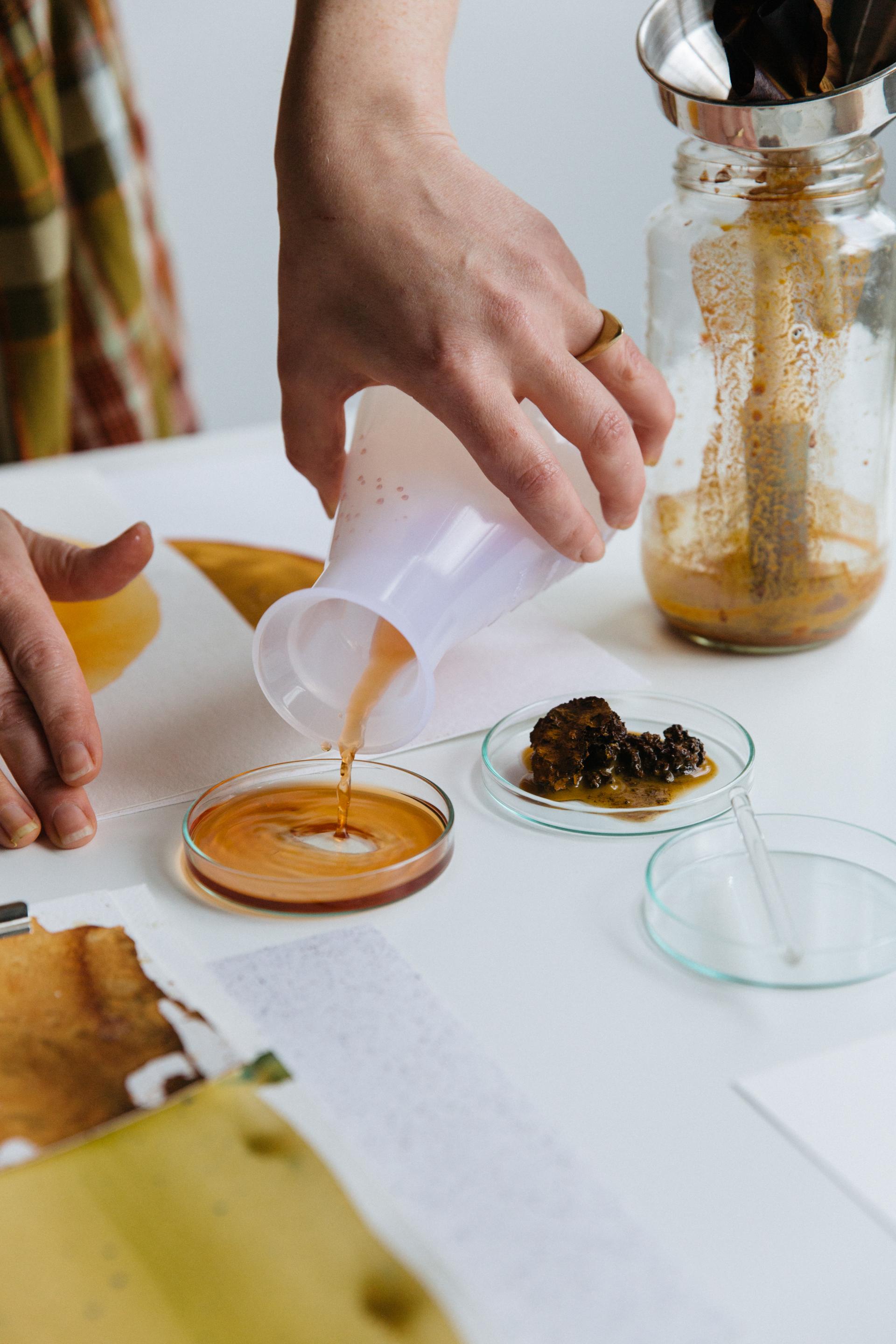A hand pours a liquid into a petri dish, showcasing materials used in sustainable color design and circularity.