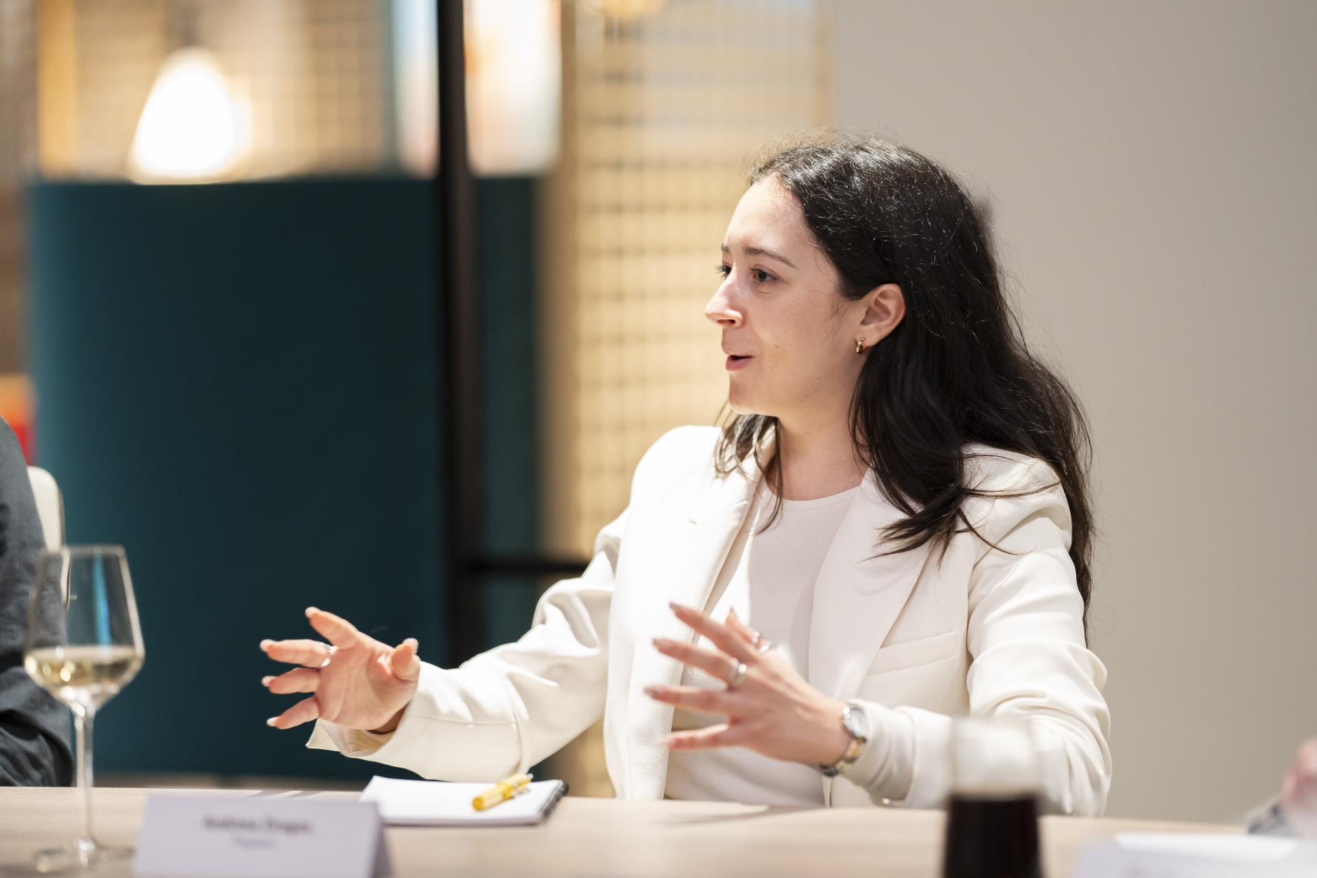 A woman in a white blazer engages in a discussion on technology and sustainability in design during a meeting.